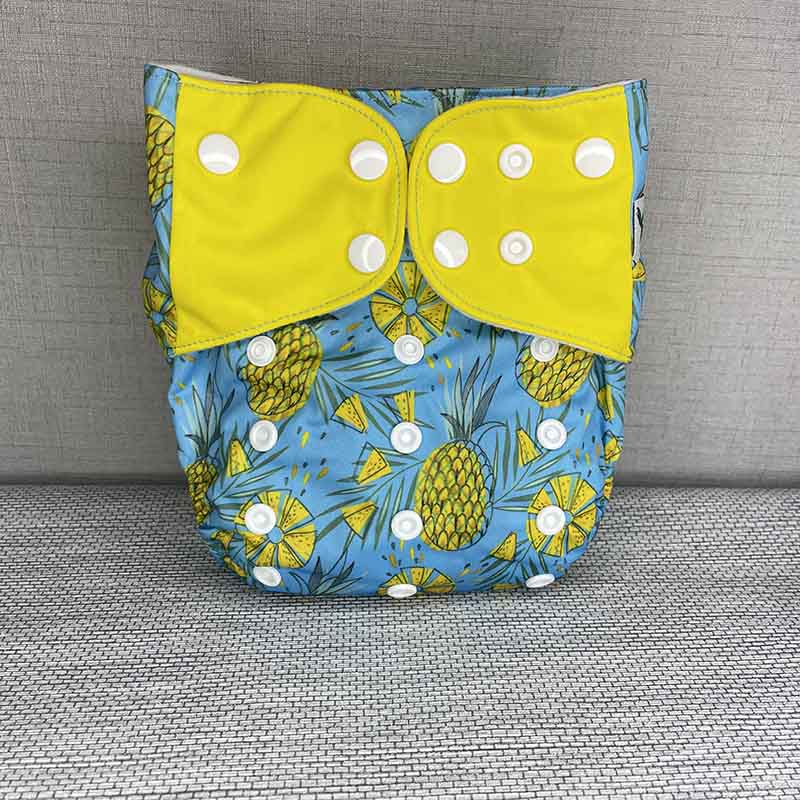 Front view of a bright cloth diaper with yellow wings, pineapples and a blue background