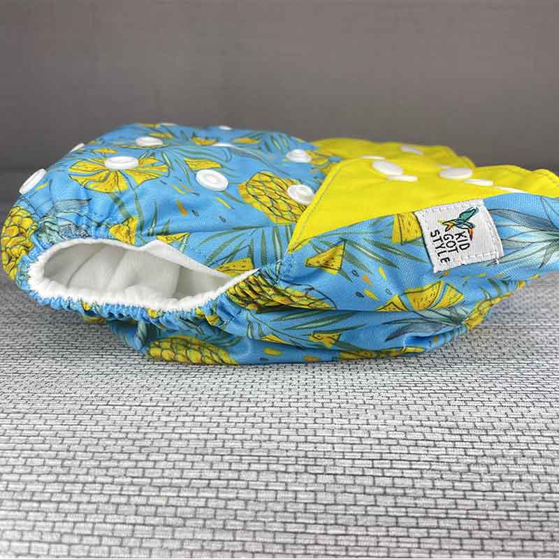 Side view of a bright cloth diaper with yellow wings, pineapples and a blue background
