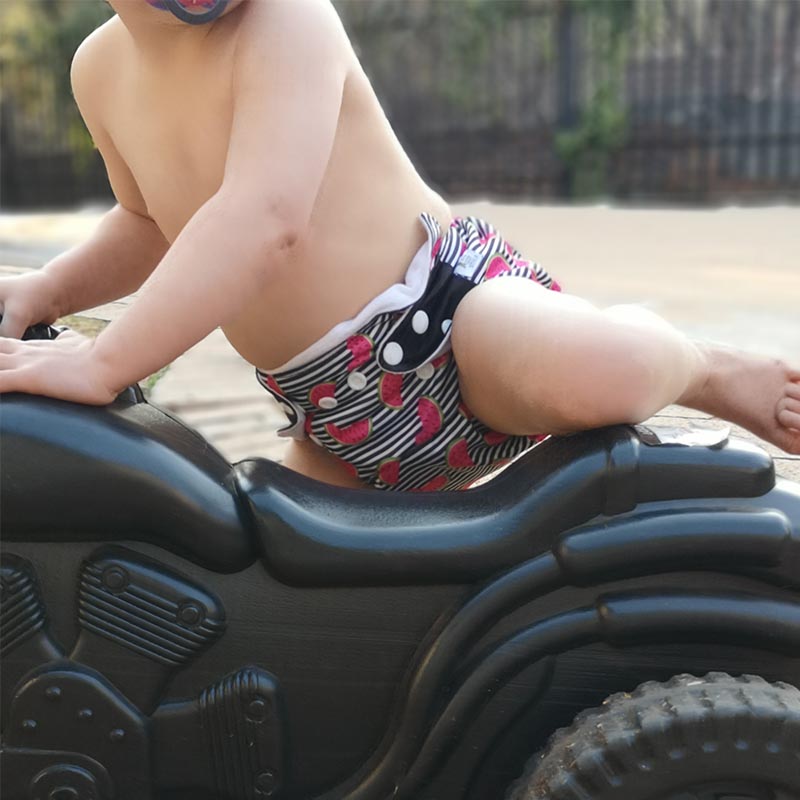 A toddler in a striped watermelon cloth nappy climbing on a bike