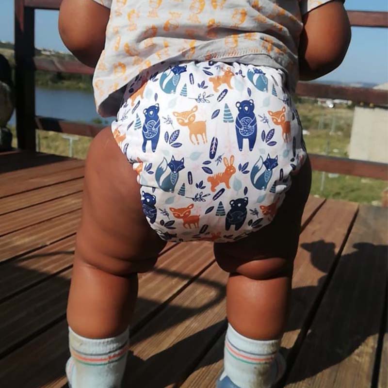 A toddler wearing a reusable cloth diaper with a woodland creatures pattern